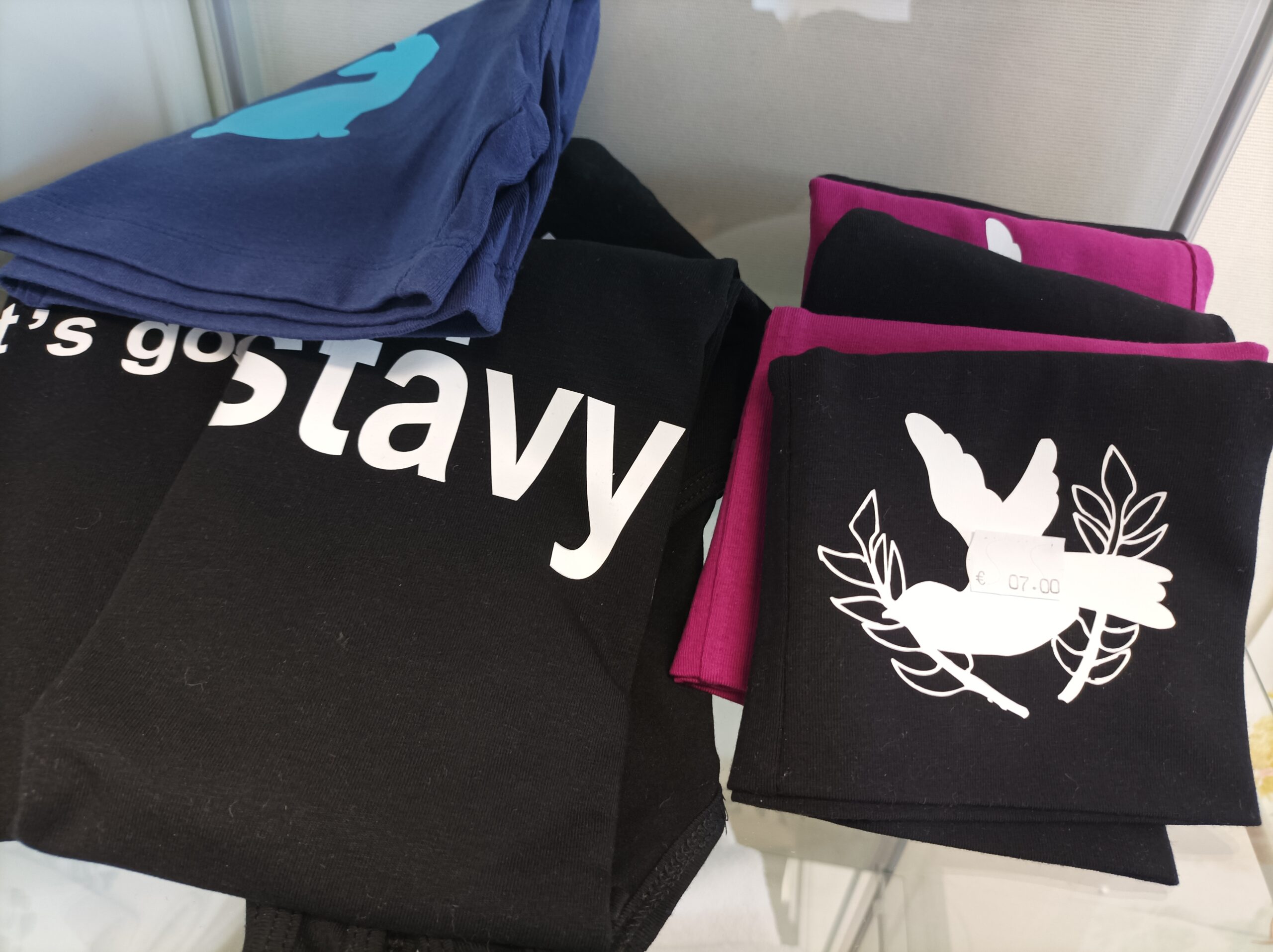 Mustia painotuotteita valkoisella painatuksella. Myös sininen painotuote sekä liiloja tuotteita.