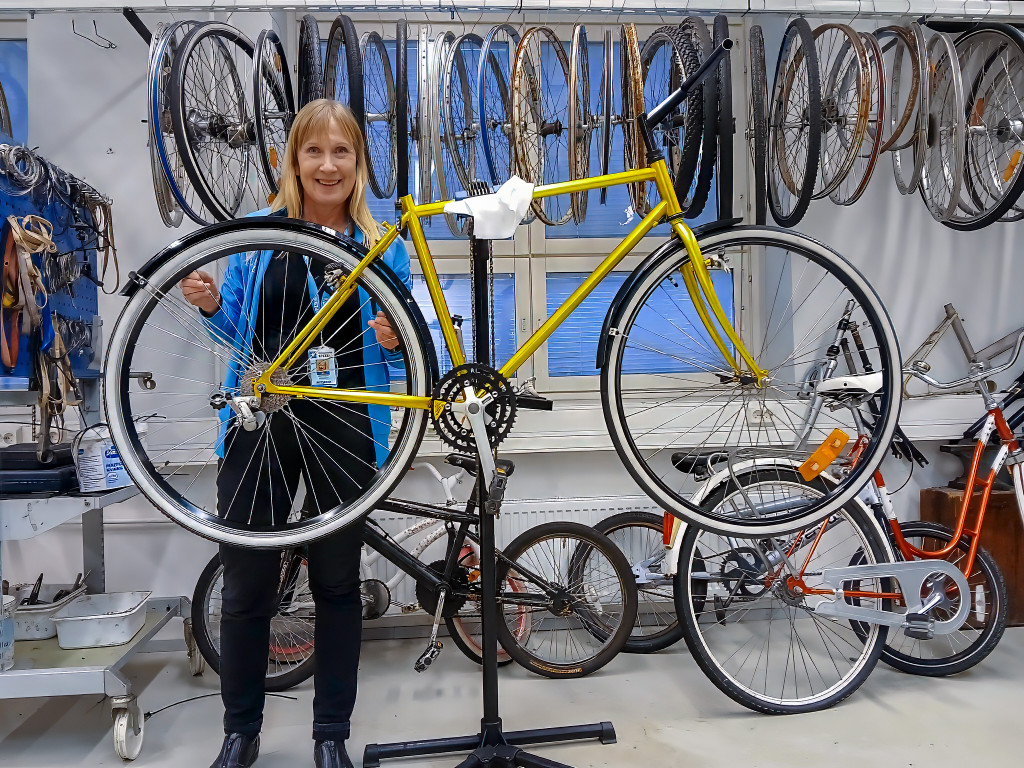 Spesian huppariin pukeutunut nainen polkypyöräkorjaamolla, korkeaan telineeseen nostetun pyörän takana.