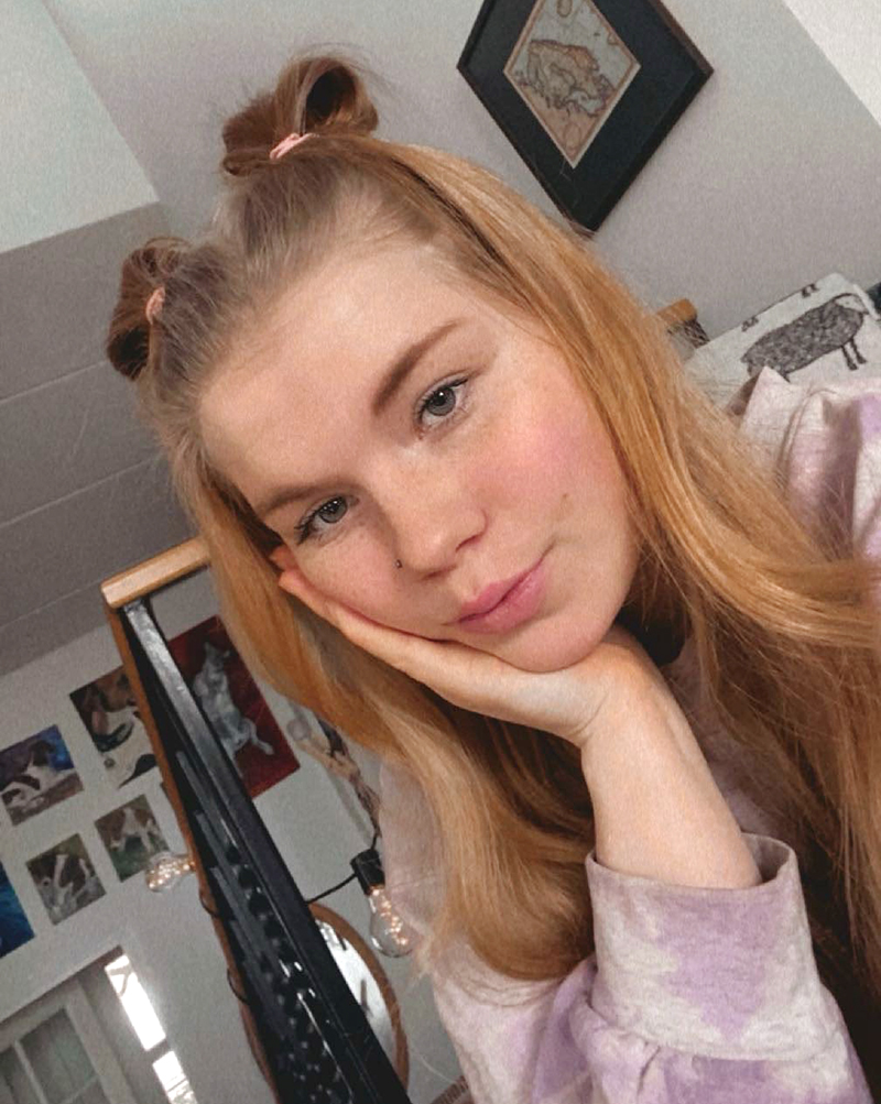 Nuori, pitkähiuksinen nainen istuu käsi poskella.