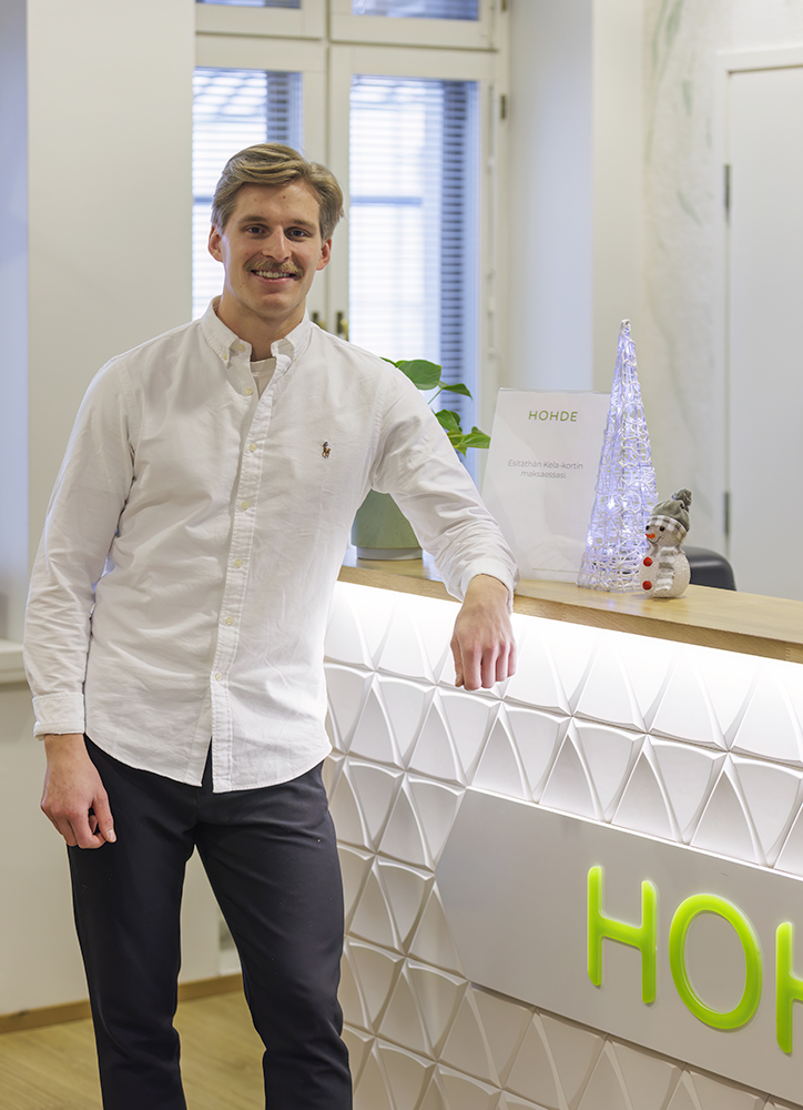 Hymyilevä mies valkoisessa kaupuspaidassa nojaa tiskiin, jossa näkyy hiukan Hammas Hohteen logoa.