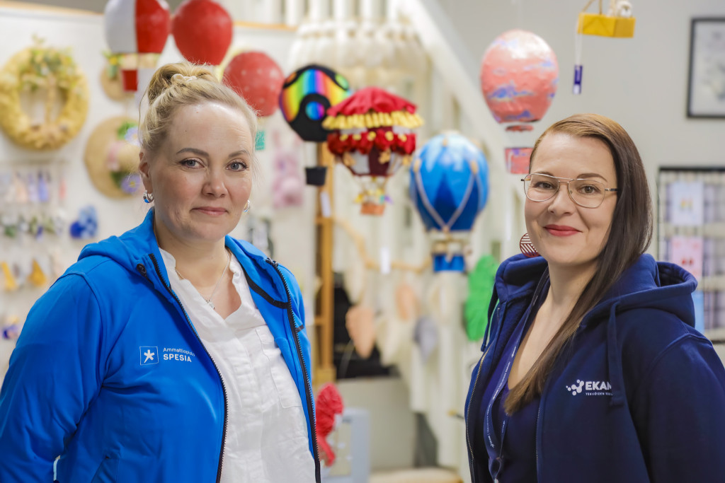 Sarita Koskinen-Soikkeli Spesian hupparissa ja Piia Andelin Ekamin hupparissa seisovat puoliksi vastakkain ja katsovat kameraa hymyillen.