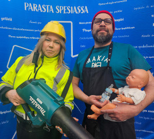 lehtipuhaltimen kanssa poseeraava nainen keltaisissa työvaatteissa ja mies, joka pitelee vauvanukkea.