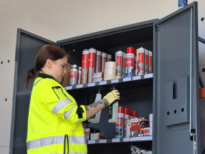 Työvaatteissa oleva Jasmin metallisen kaapin edessä, jossa on erilaisia tuotteita.