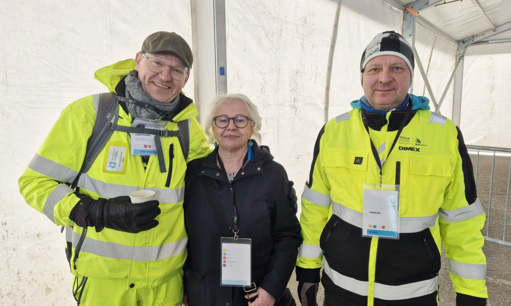 Kolme Spesian työntekijää Taitaja-teltassa: keltaisiin huomiovaatteisiin pukeutunutta miestä ja heidän välissään tummaan takkiin pukeutunut nainen.