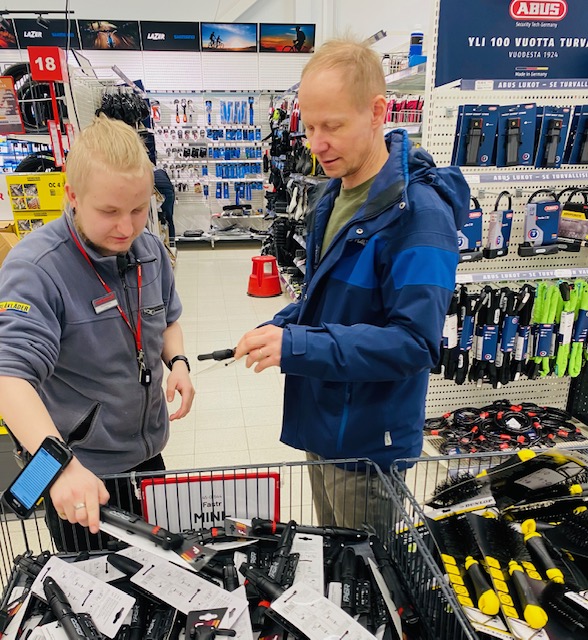 Kaksi miestä katsoo työkaluja kaupassa, tummansiniset työvaatteet päällä.