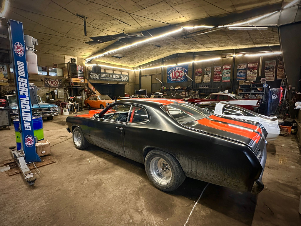 Autokerhon sisätila, jossa on useita klassikkoautoja. Etualalla musta auto, jossa on oranssit raidat. 