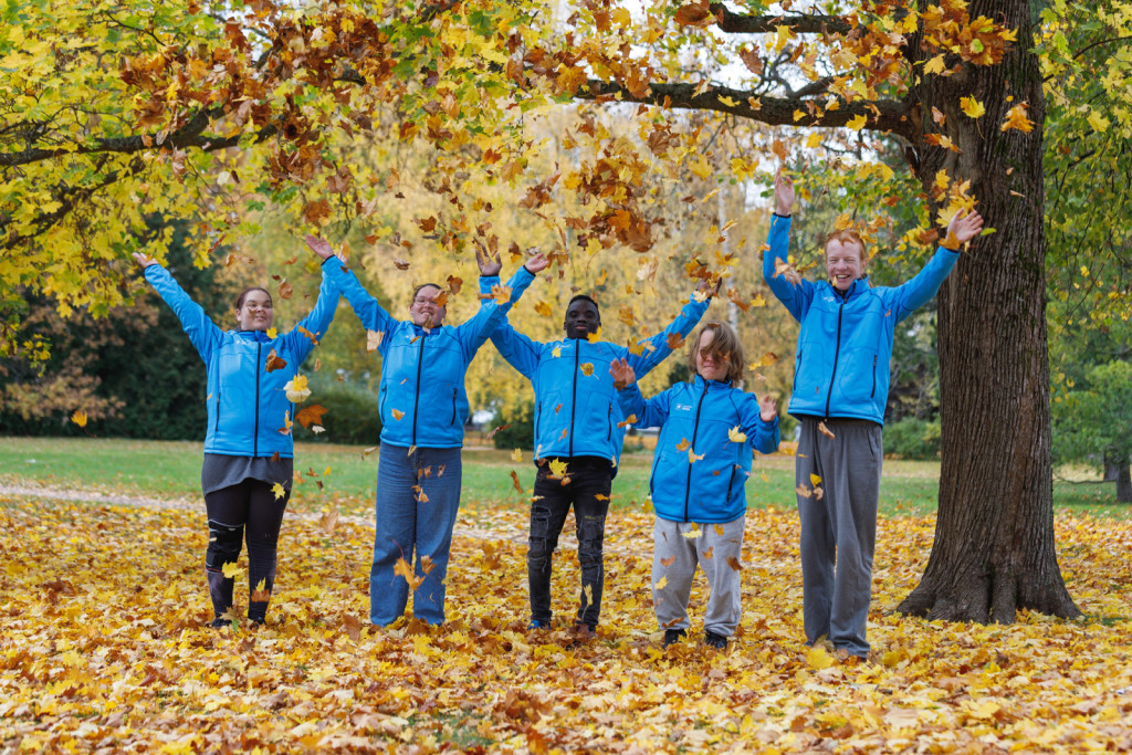 Viisi nuorta Spesian takit päällä syksyisessä maisemassa heittävät keltaisia lehtiä ilmaan.