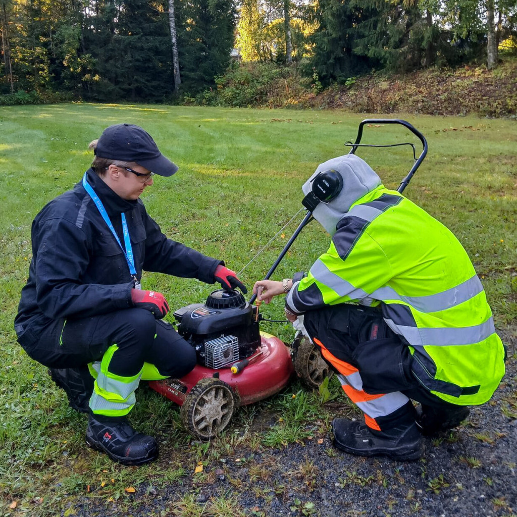 Kaksi miestä tutkii ruohonleikkuria pihalla.