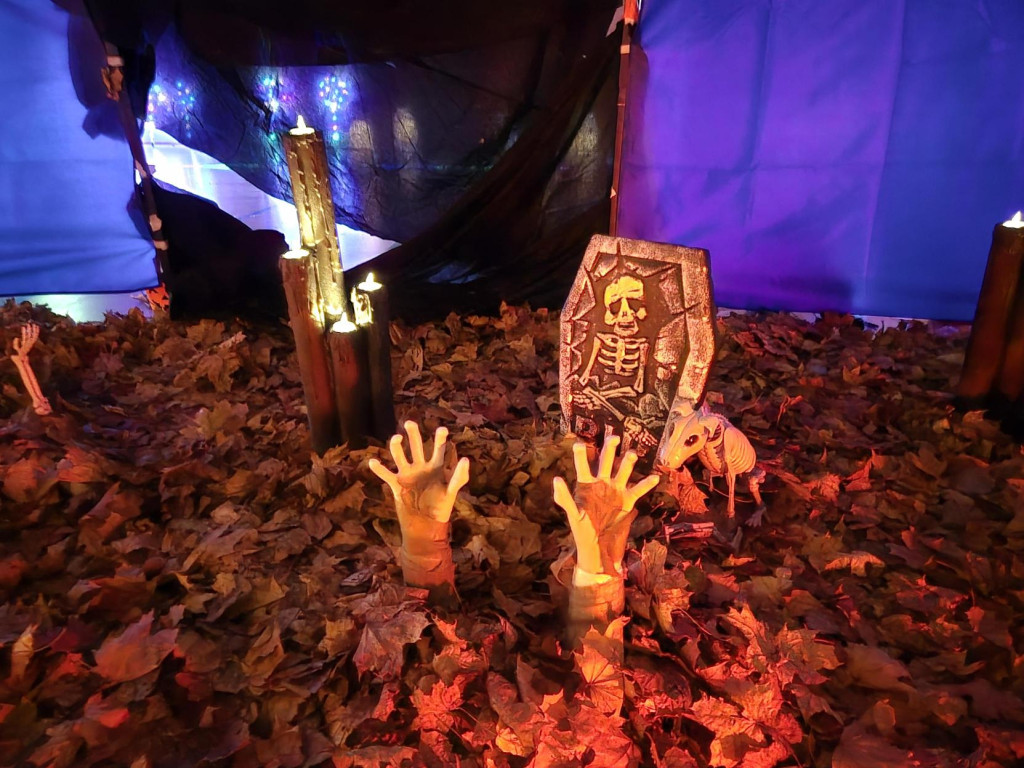 Halloween-koristeita maassa. Kädet, jotka kurkottavat lehtien seasta ja hautakivi. 