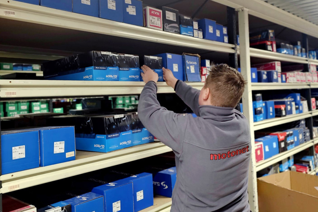 Mies hyllyttää varaosia, päällä Motonetin takki.
