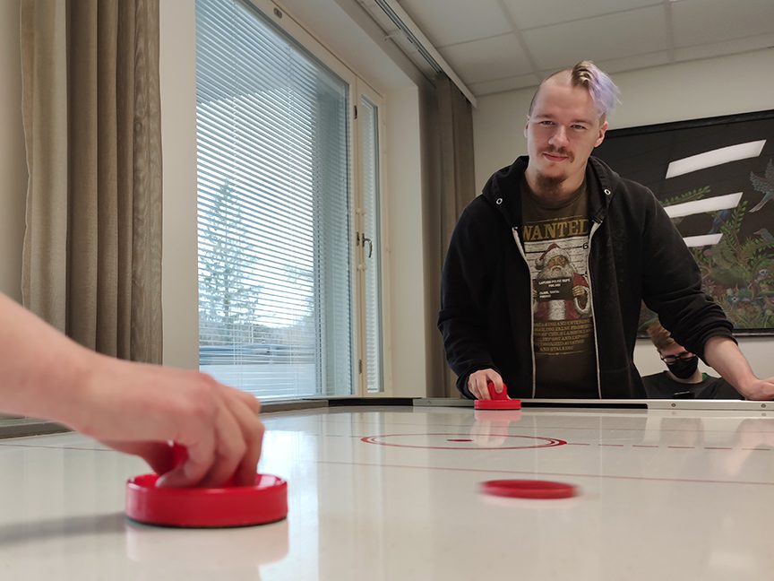 Kaksi nuorta pelaa liitokiekkoa pöydällä, paikka on asuntolan yhteinen oleskelutila.