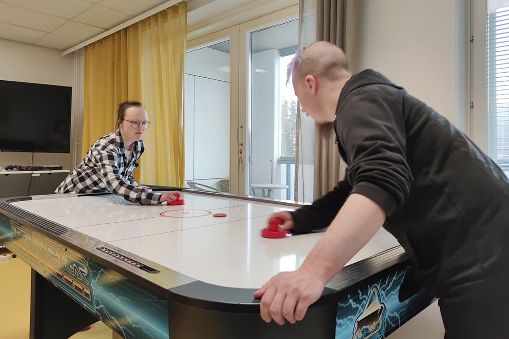 Kaksi nuorta pelaa liitokiekkoa pöydällä, paikka on asuntolan yhteinen oleskelutila.