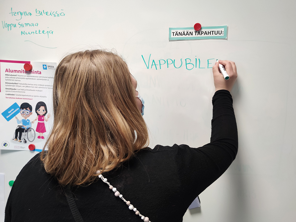 Takaapäin näkyvä henkilö kirjoittaa valkotaululle "vappubileet".