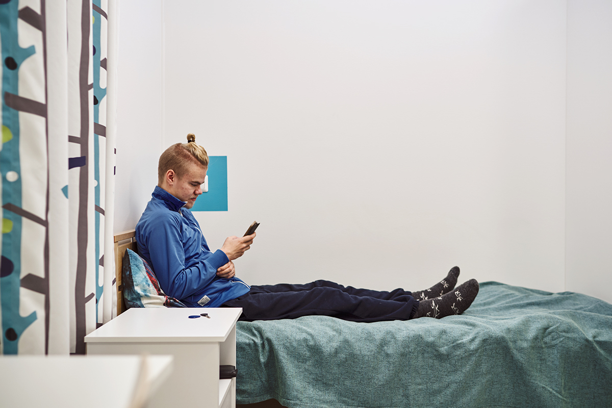 Nuori mies istuu sängyllä ja katsoo kännykkää.