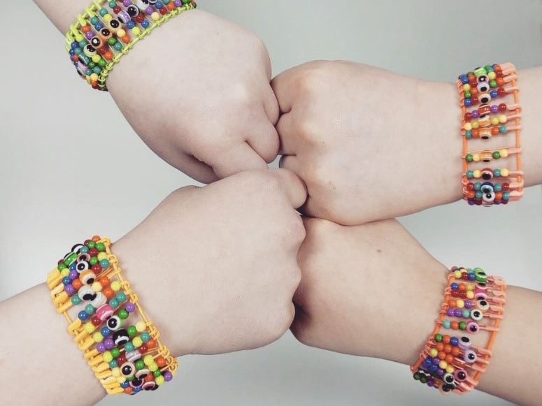 Neljä nyrkkiä yhteen painettuna, ranteissa samanlaiset helmirannekkeet.