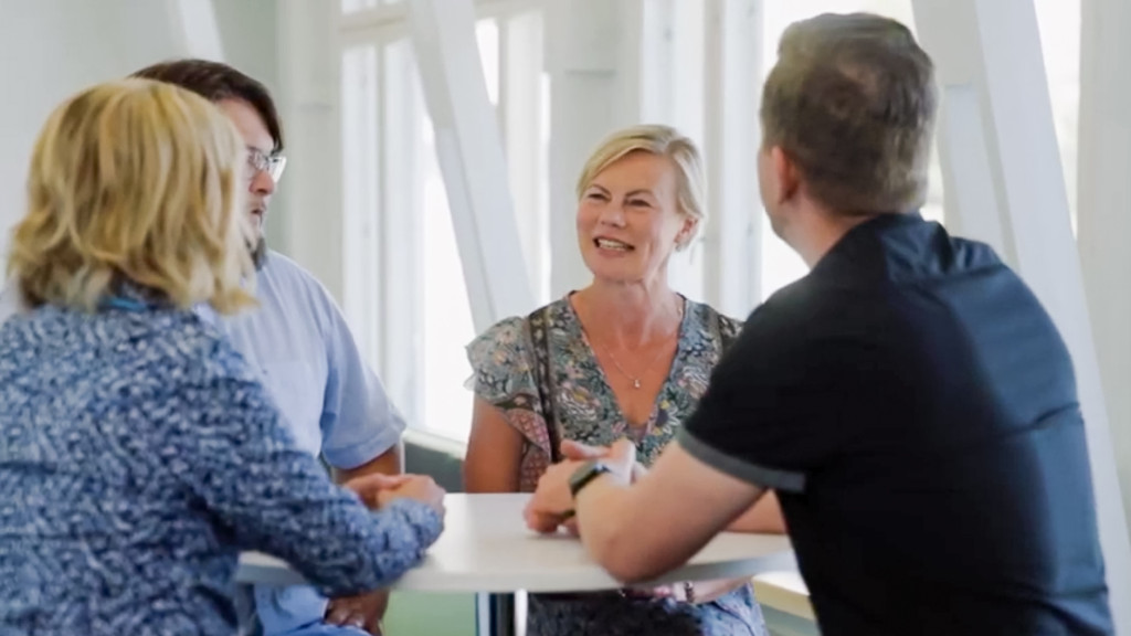 Neljän henkilön porukka keskustelemassa pöydän ympärillä.