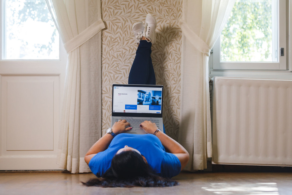 Henkilö makaa lattialla jalat ylhäällä seinää vasten tietokone sylissään.