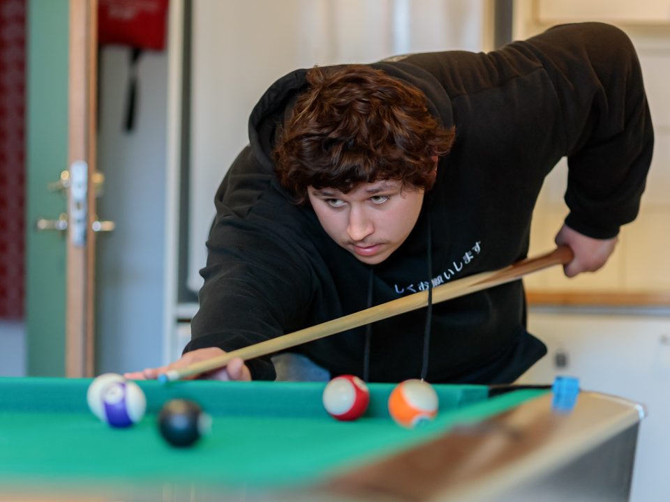 Poika kumartuneena pelaamaan biljardia.