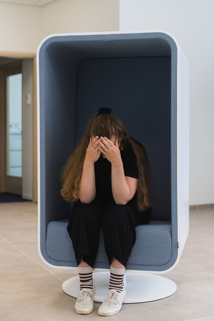 Pitkähiuksinen henkilö istuu etukumarassa kädet kasvojen edessä kuutiotuolissa.