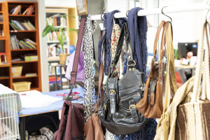 Laukkuja ja huiveja vaatetangolla, taustalla kirjahyllyjä.