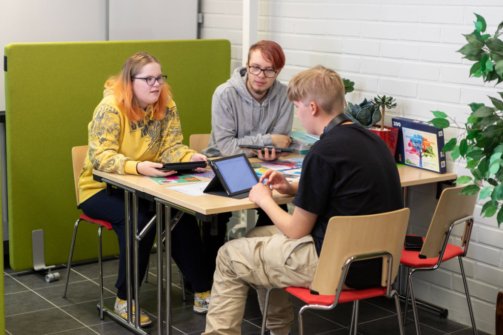 Kolme opiskelijaa keskustelee pöydän äärellä.