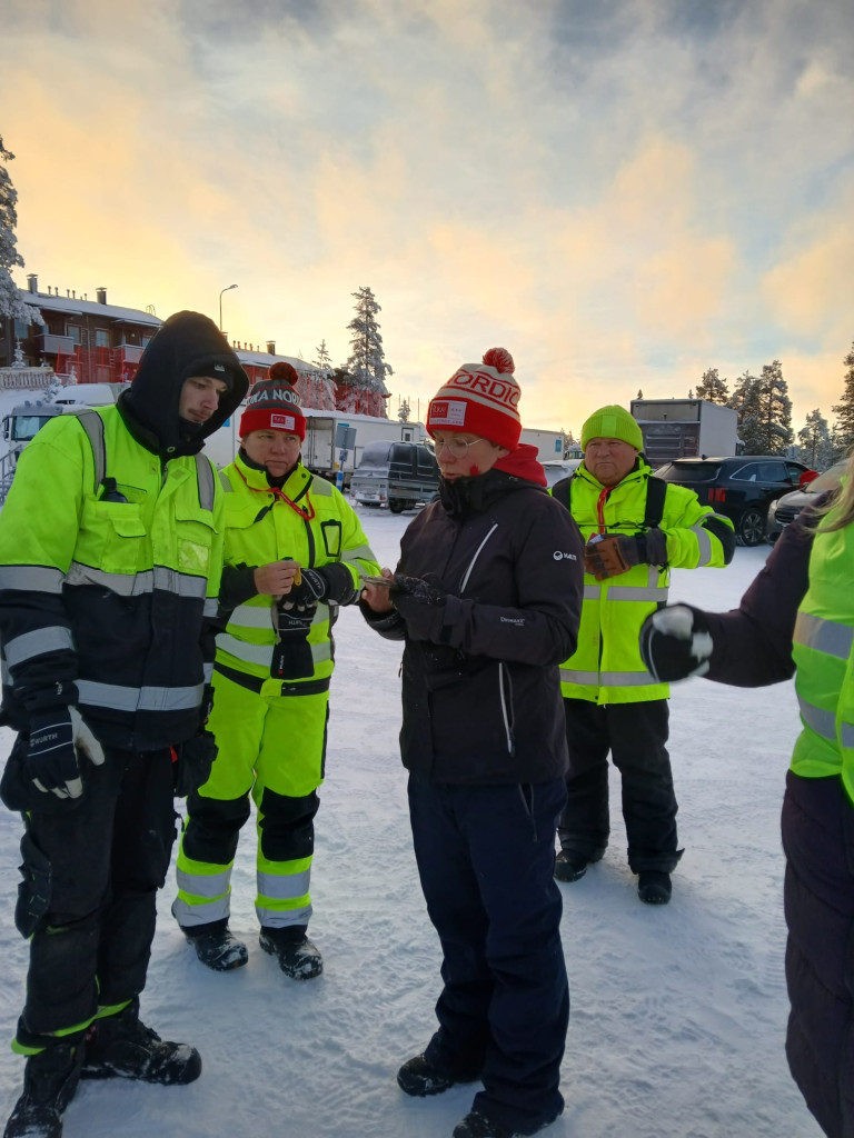 Opiskelijoita työvaatteet yllään ulkona kuulemassa ohjeita työtehtäviin liittyen. 