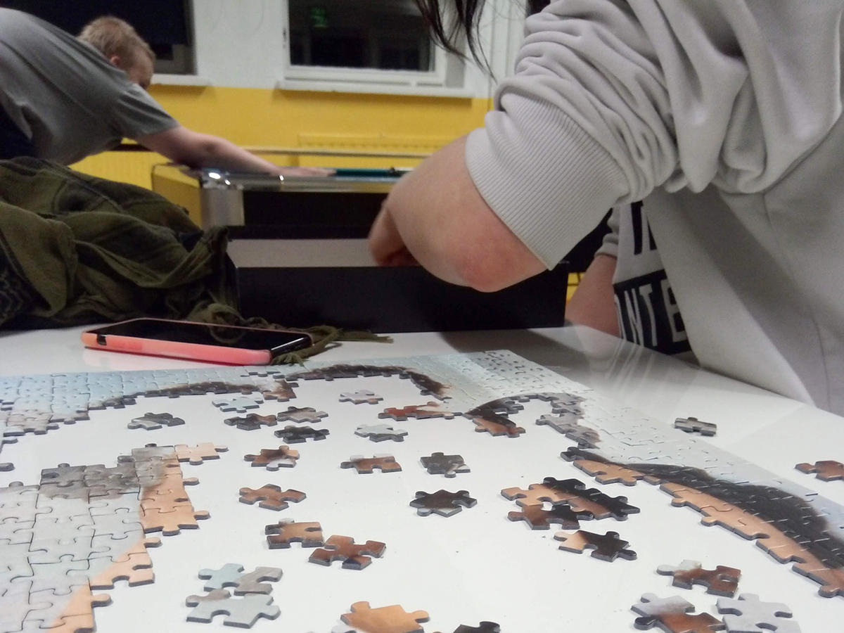 Keskeneräinen palapeli pöydällä, takana biljardin pelaajia.